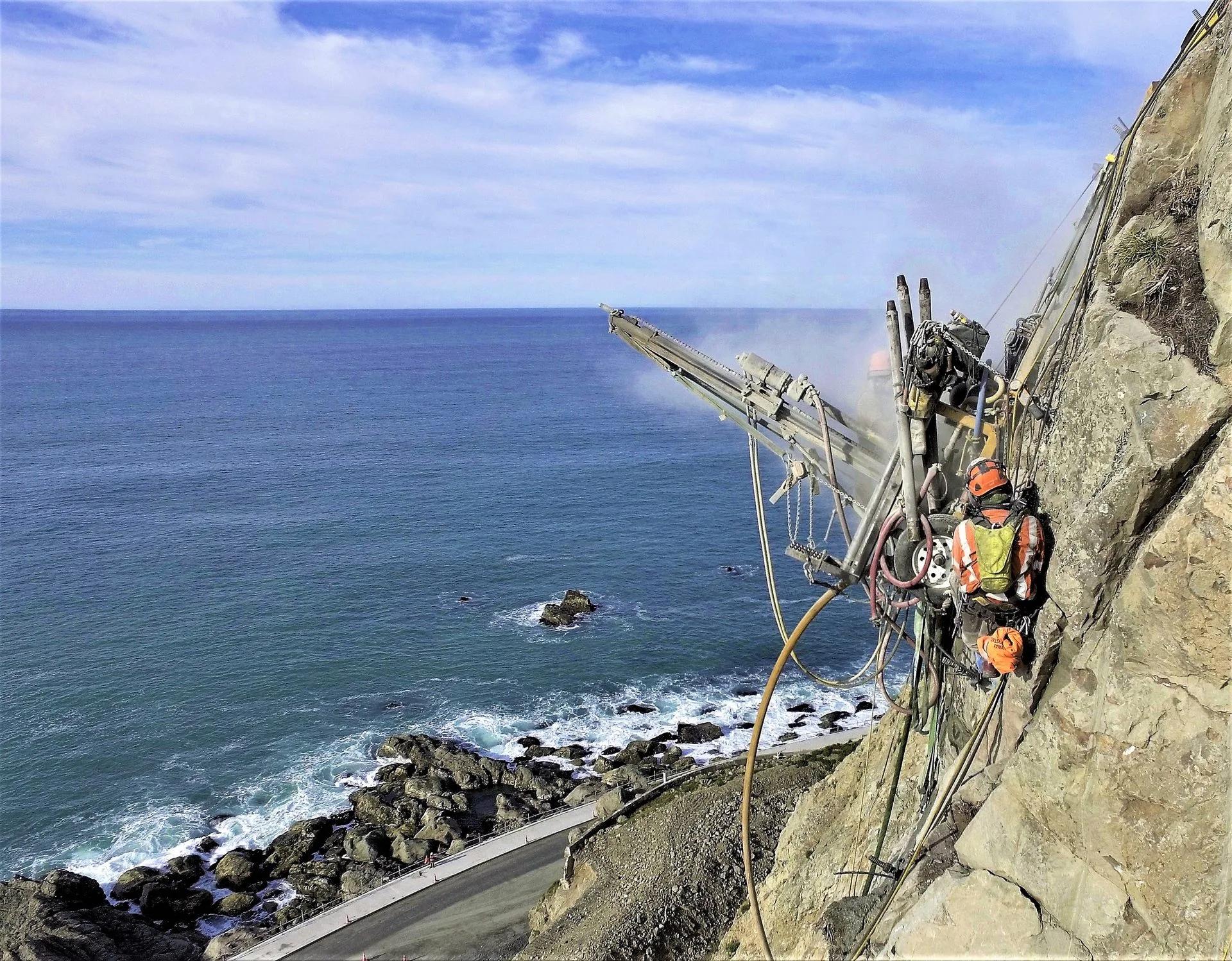 Rope access crew drilling a steep coastal rock slope in New Zealand